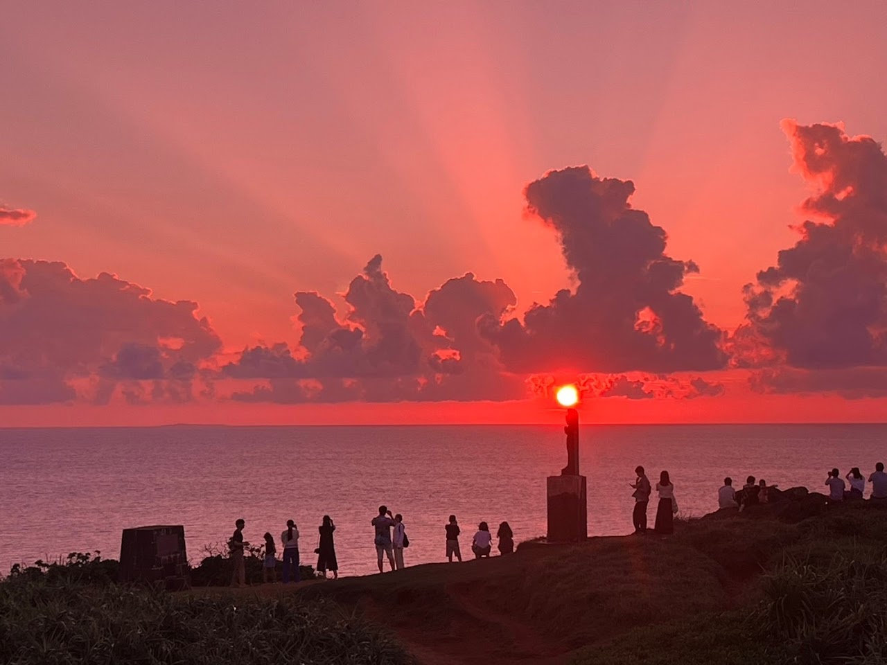 真紅の夕日を眺める海辺の人々と雲のシルエット
