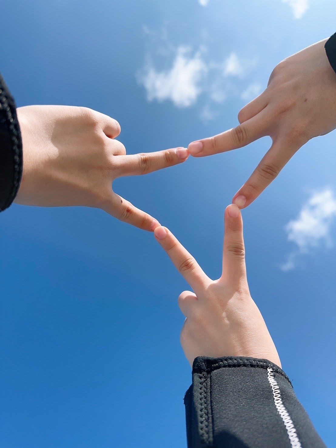青空の下で三人の指先を合わせて作った三角形